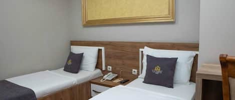 Una habitación de hotel con dos camas individuales, un cabecero de madera, una mesita de noche con teléfono y control remoto, y un cuadro enmarcado en la pared.