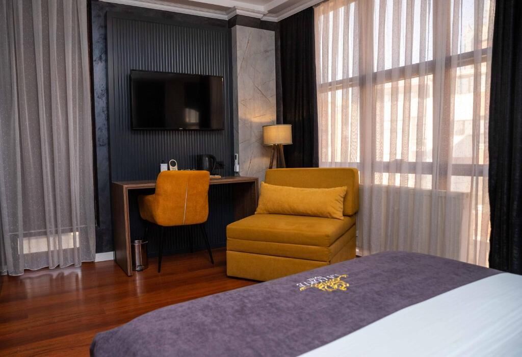 A hotel room with a bed, a desk, a chair, a TV, and a window with curtains.