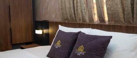 A hotel room with a bed, two pillows with a logo, a nightstand, a lamp, and curtains.
