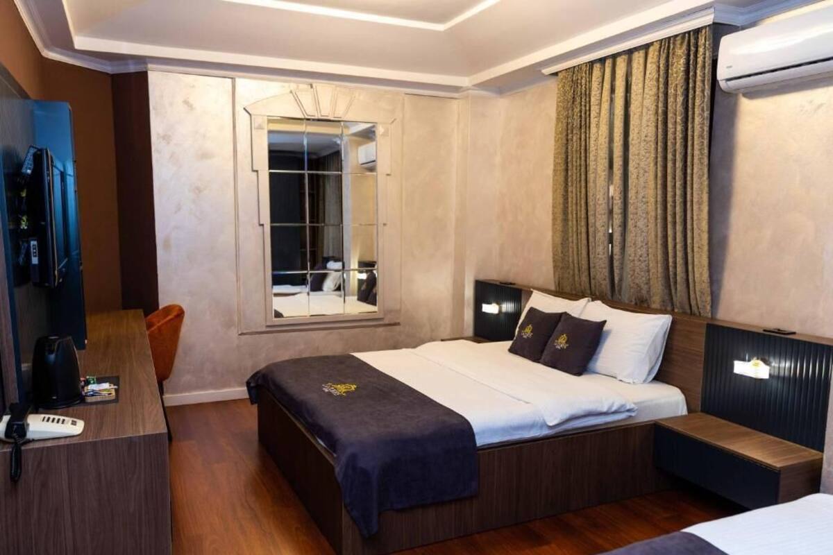Une chambre d’hôtel comprenant un lit, une table de chevet, un bureau avec un téléphone, un miroir et une fenêtre avec des rideaux.