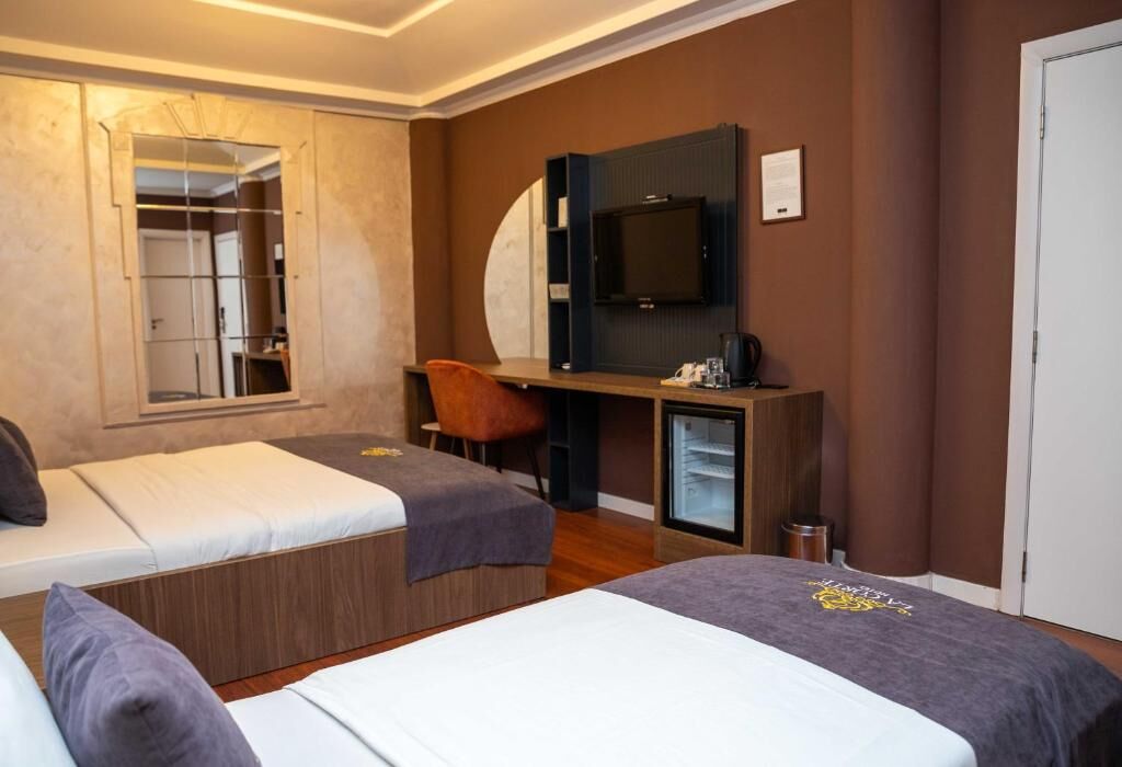 A hotel room with two beds, a desk, a TV, and a mirror.