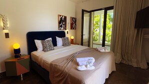 A hotel room with a bed, pillows, a nightstand, a lamp, a towel, and a view of greenery through a glass door. - Carthage Villa 3BR Luxury Pool Garden (Carthage)