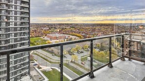 A high-rise building with a balcony, a cityscape view, and a cloudy sky. - Modern 2BR+Den Condo near Square One | Sleeps 6 | Mins to Pearson YYZ (Mississauga)