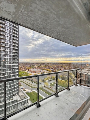 A high-rise building with a balcony, a cityscape view, and a cloudy sky.