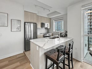 A modern kitchen with a central island, stainless steel appliances, and a view of a cityscape through a large window.