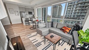 A modern living room with a sofa, coffee table, and a dining area with chairs and a table. - Modern 2BR+Den Condo near Square One | Sleeps 6 | Mins to Pearson YYZ (Mississauga)