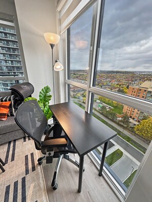A modern office space with a large window, a desk, a chair, and a lamp.