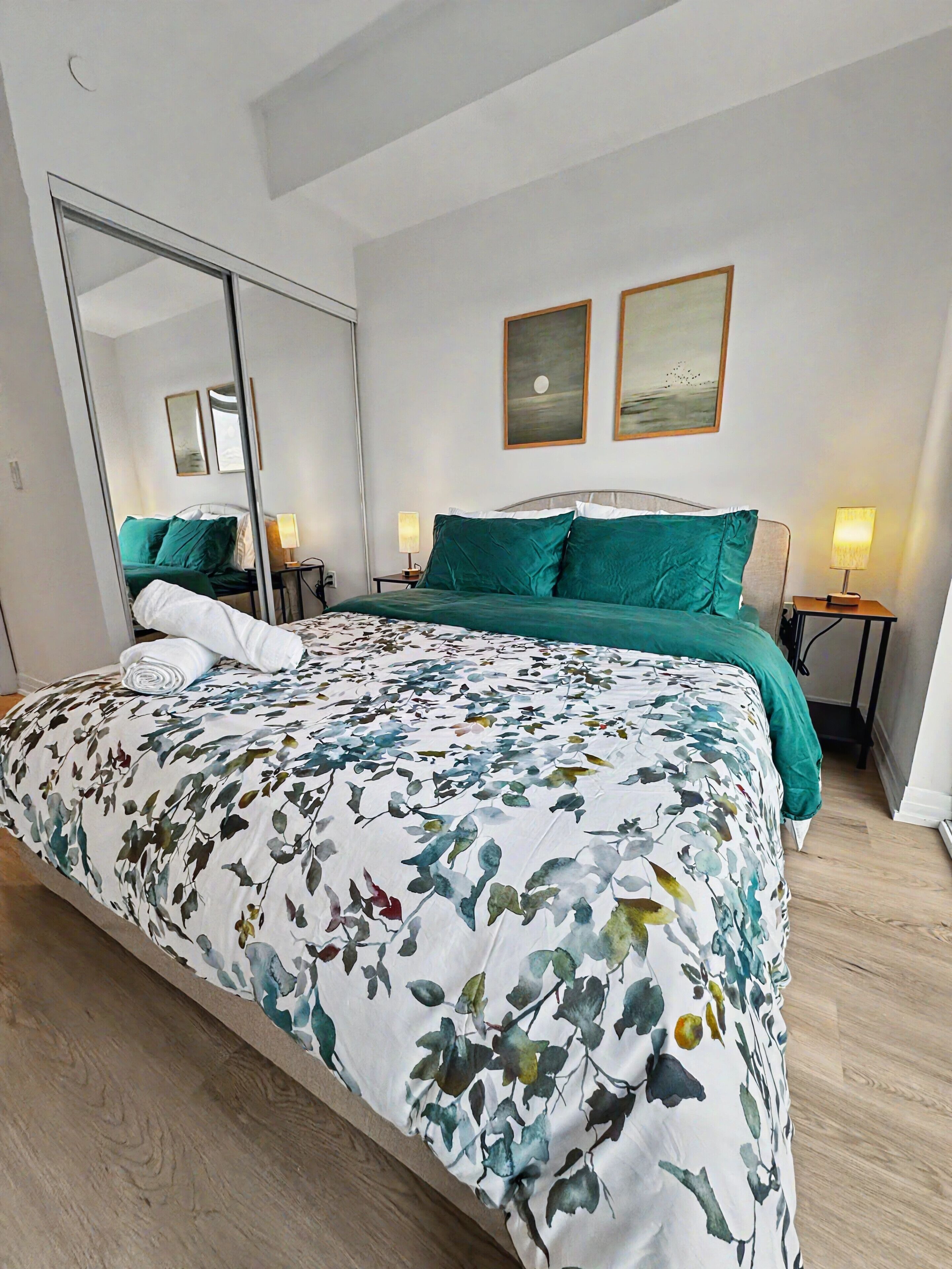 Une chambre à coucher avec un grand lit, un miroir en pied, deux lampes de chevet et deux tableaux encadrés accrochés au mur.