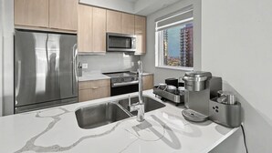 A modern kitchen with stainless steel appliances, a marble countertop, and a window with a city view. - Modern 2BR+Den Condo near Square One | Sleeps 6 | Mins to Pearson YYZ (Mississauga)