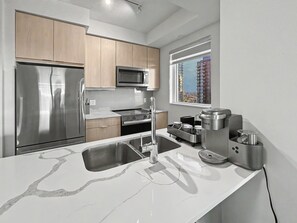 A modern kitchen with stainless steel appliances, a marble countertop, and a window with a city view.