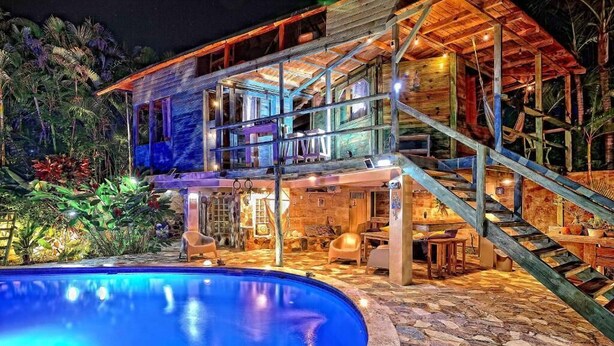 Una casa de madera de varios niveles con piscina, mobiliario exterior y una escalera.