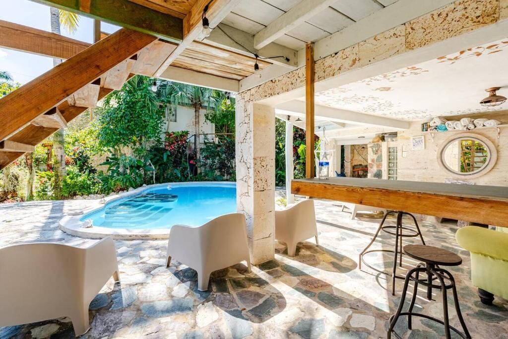 A pool area with stone flooring, white bar stools, and a bar counter.
