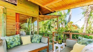 Una terraza de madera con un sofá y una mesita, rodeada de exuberante follaje tropical.
