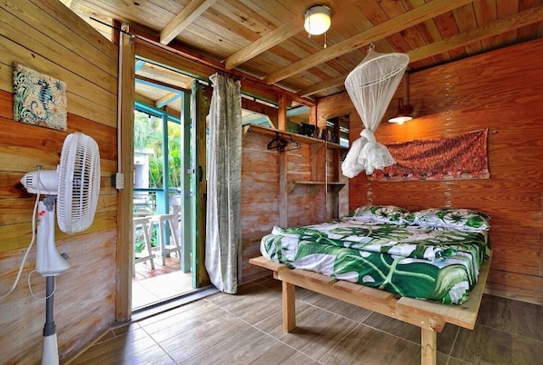 A wooden room with a bed, a fan, and a mosquito net.