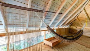 Una hamaca en una habitación de madera con techo inclinado y vistas al verdor exterior.