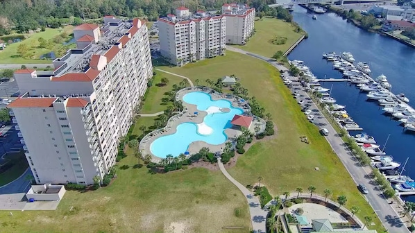 Ein Hochhaus-Hotel mit mehreren Balkonen, einem zentralen Schwimmbecken und einer Marina mit Booten.