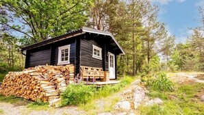 A small cabin with a wooden exterior, a porch, and a stack of firewood. - Ekhaga Cabins - Holiday home by the Baltic Sea with sauna & nature (Dröstorp)