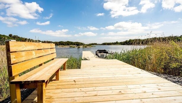 A wooden dock leading to a calm lake with a bench and a boat. - Ekhaga Cabins - Holiday home by the Baltic Sea with sauna & nature (Dröstorp)