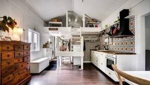 A spacious kitchen with white cabinetry, a wooden dresser, and a dining area with a white table and chair. - Ekhaga Cabins - Holiday home by the Baltic Sea with sauna & nature (Dröstorp)