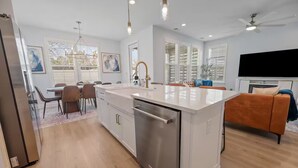 Une cuisine moderne avec un îlot central, un coin repas avec des chaises, un canapé et un téléviseur à écran plat.