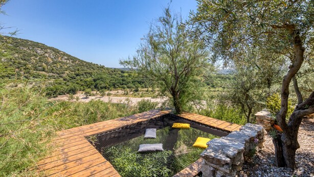 A hot tub with a wooden deck, surrounded by olive trees and a hilly landscape.
