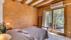 A bedroom with a bed, a nightstand, a lamp, a ladder, and a view of the outdoors.