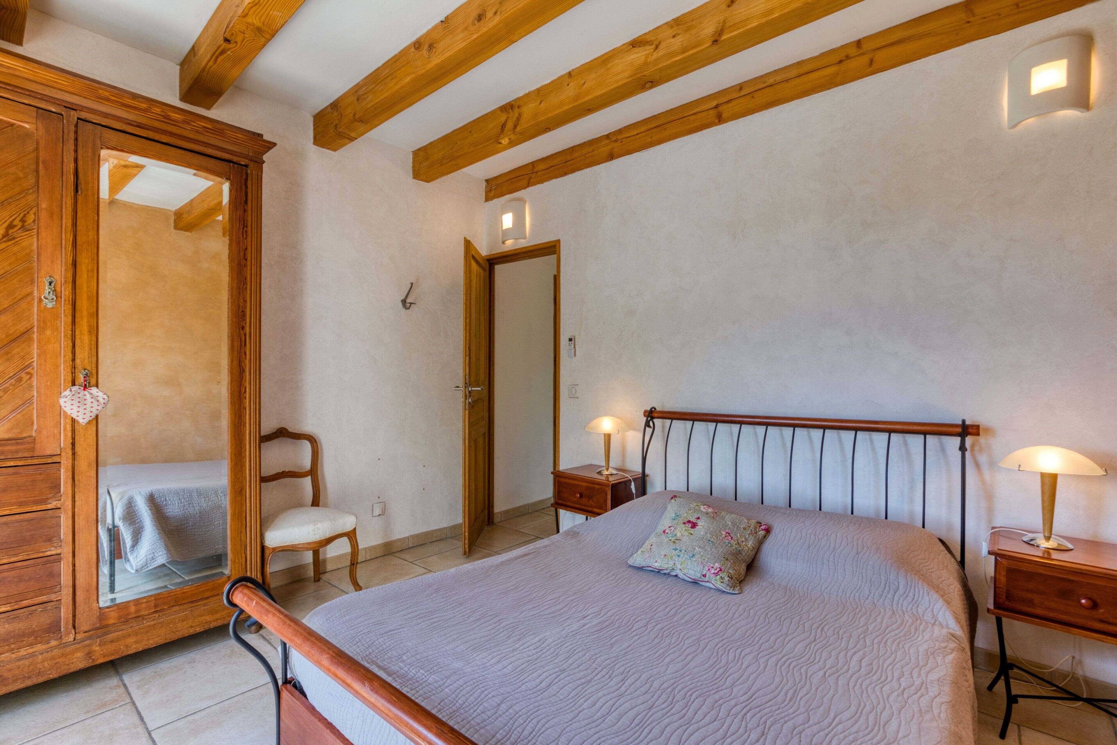 Een slaapkamer met een bed, een houten garderobe, nachtkastjes en een spiegel.