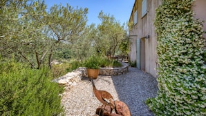 A courtyard with a stone wall, a metal sculpture, and a building with climbing plants.