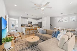 Ein modernes Wohnzimmer mit Sofa, Couchtisch und Fernseher. Es gibt eine Küchenzeile mit Esstisch und Stühlen.