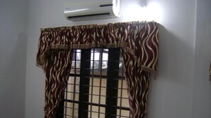 Una habitación con ventana de diseño cuadriculado, una silla, una mesita y un equipo de aire acondicionado.