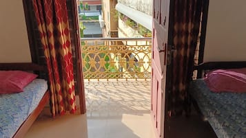 A room with two beds, each with a pink pillow, and a balcony with a decorative railing.