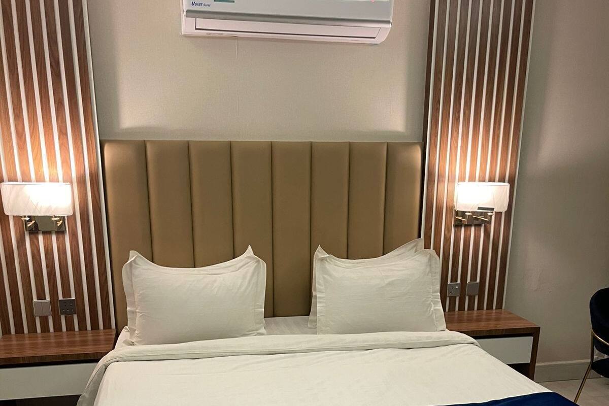 Hotellihuone, jossa on suuri sänky, kaksi yöpöytää, ilmastointilaite ja seinään kiinnitetyt lamput.