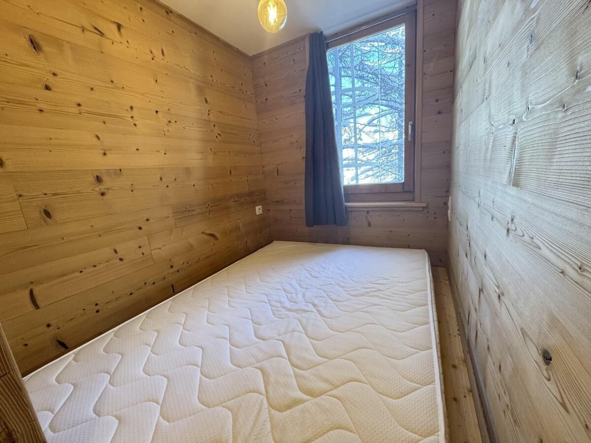 Um quarto pequeno de madeira com uma cama, uma janela com vista para árvores e uma luminária no teto.