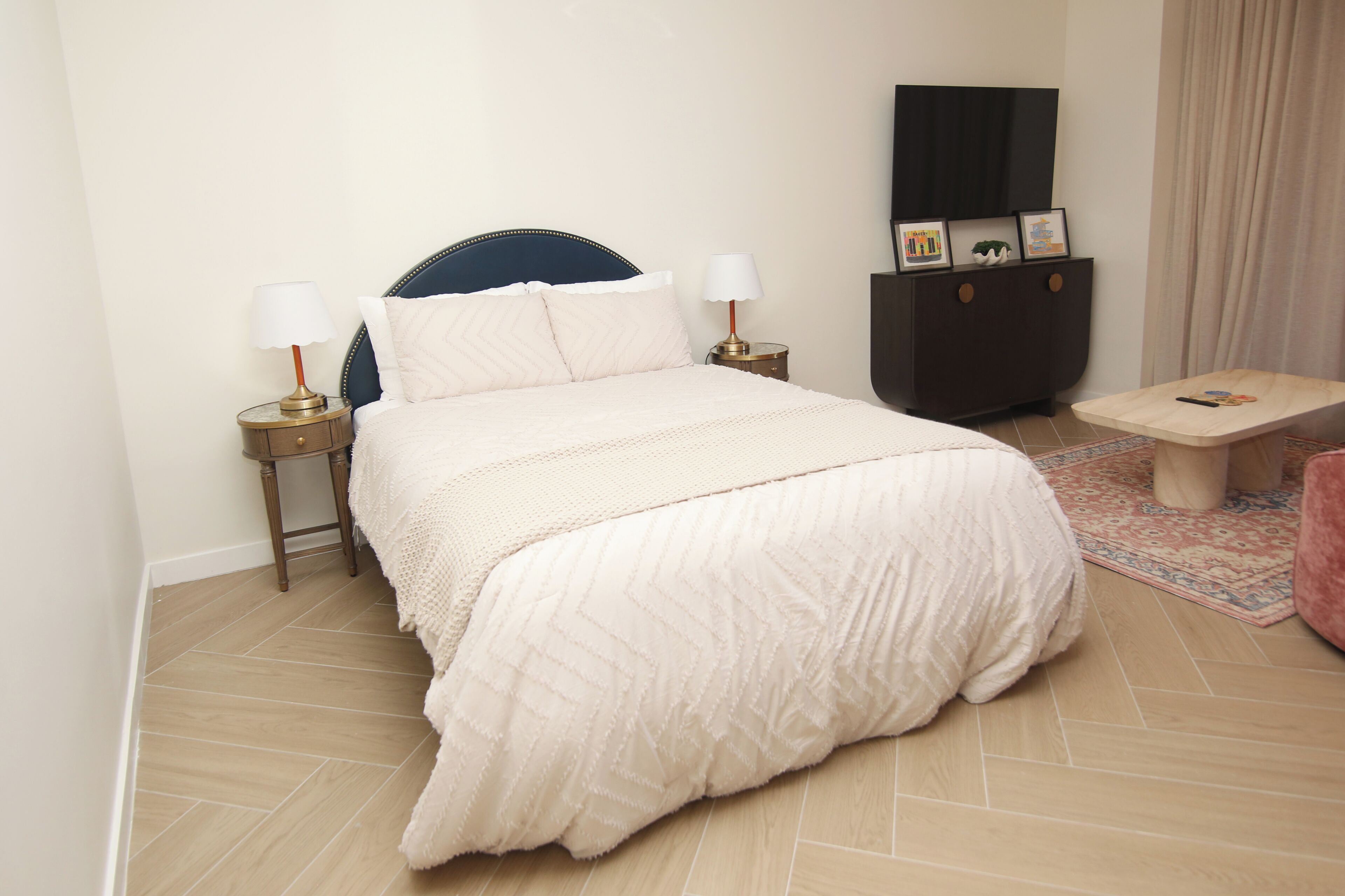 A neatly arranged hotel room with a bed, bedside tables, a small table, a cabinet, and a TV.