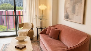 A modern living room with a curved sofa, a coffee table, a floor lamp, and a large window with a view of buildings. - Stylish Residences Wynwood (Miami)
