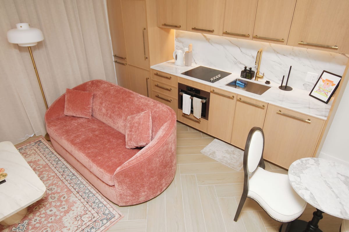 Un espace de vie compact comprenant un canapé, une table à manger, une chaise, un petit coin cuisine avec un évier et une cuisinière, et une lampe sur pied.