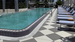 A pool area with lounge chairs, a tiled floor, and a building with a distinctive arched entrance. - Stylish Residences Wynwood (Miami)