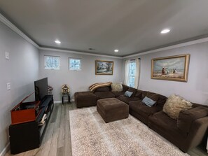 A living room with a sectional sofa, a flat-screen TV, a vintage radio, and two framed paintings.