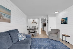 A modern living room with a gray sofa, a blue patterned rug, a gray armchair, and a small wooden side table. - Direct Oceanfront Condo with Stunning Views! (Myrtle Beach)