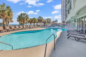 A pool area with lounge chairs, palm trees, and a building with large windows. - Direct Oceanfront Condo with Stunning Views! (Myrtle Beach)