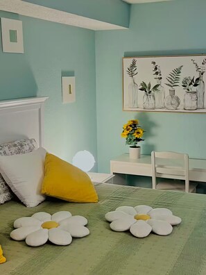 Un dormitorio con cama, almohadas, un escritorio, una silla y una obra de arte en la pared.