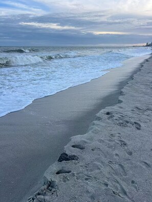 Una playa con olas, un muelle al fondo y huellas en la arena.