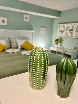 Un cactus y un florero verde sobre una mesa en una habitación con una cama y un cuadro en la pared.