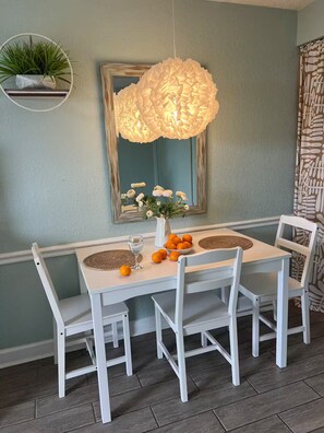 Comedor con una mesa blanca, sillas, lámpara colgante, espejo y planta en maceta.
