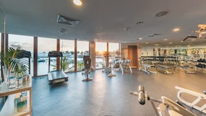 Un gimnasio con equipo de ejercicio, ventanas amplias y vista al océano.