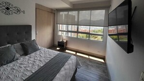 Een slaapkamer met een bed, een televisie, een raam en een nachtkastje.