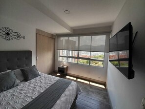Ein Schlafzimmer mit einem Bett, einem Fernseher, einem Fenster und einem Nachttisch.
