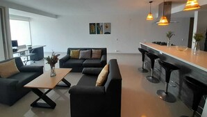Een moderne woonkamer met een zithoek, een salontafel en een keuken met een bar.