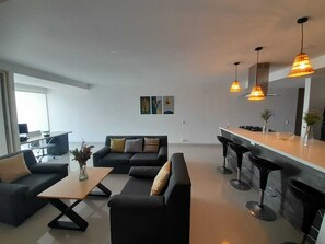 Ein modernes Wohnzimmer mit einer Sofagarnitur, einem Couchtisch und einer Küchenzeile mit Bar.
