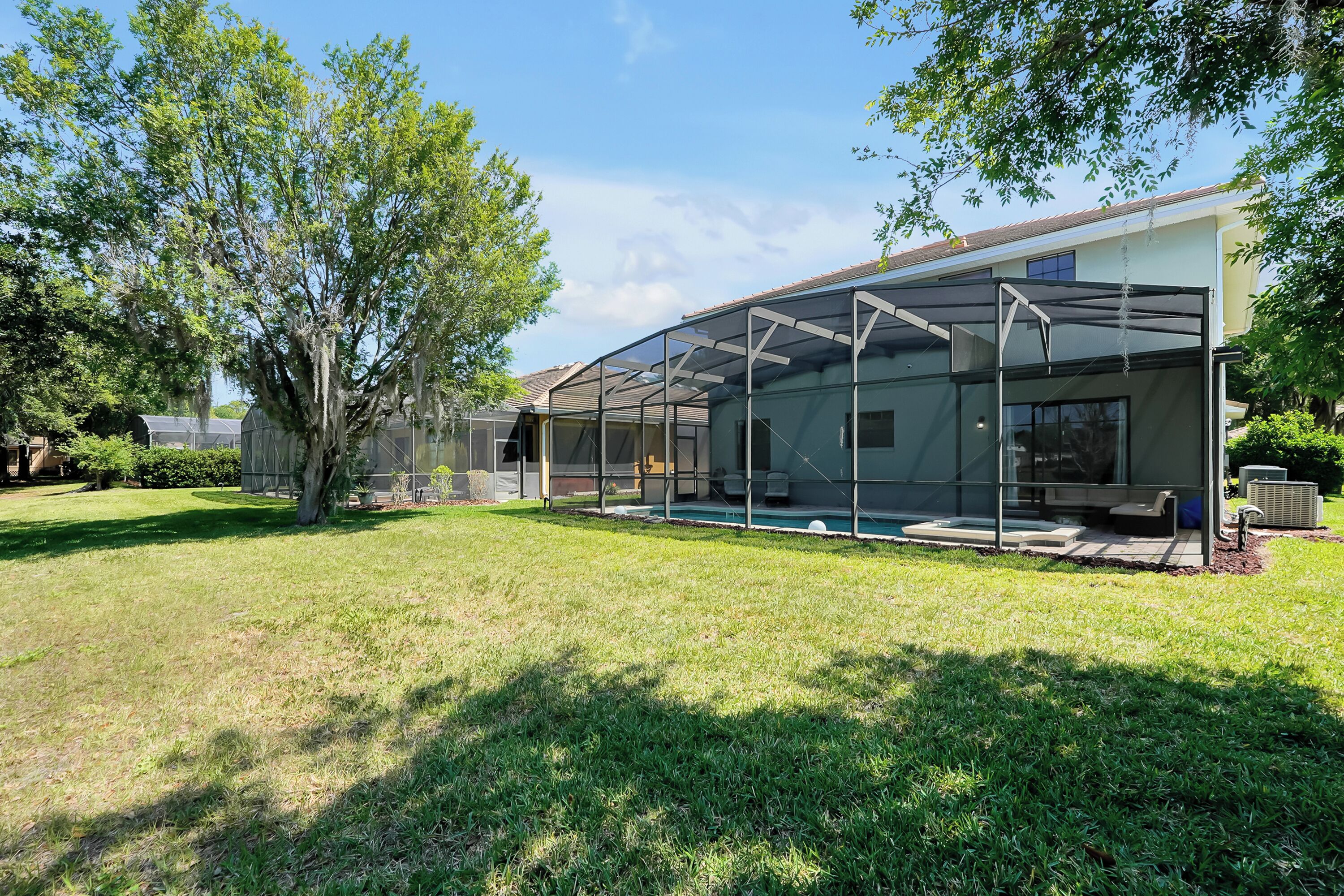 A modern house with a glass-enclosed patio, a swimming pool, and a well-maintained lawn.